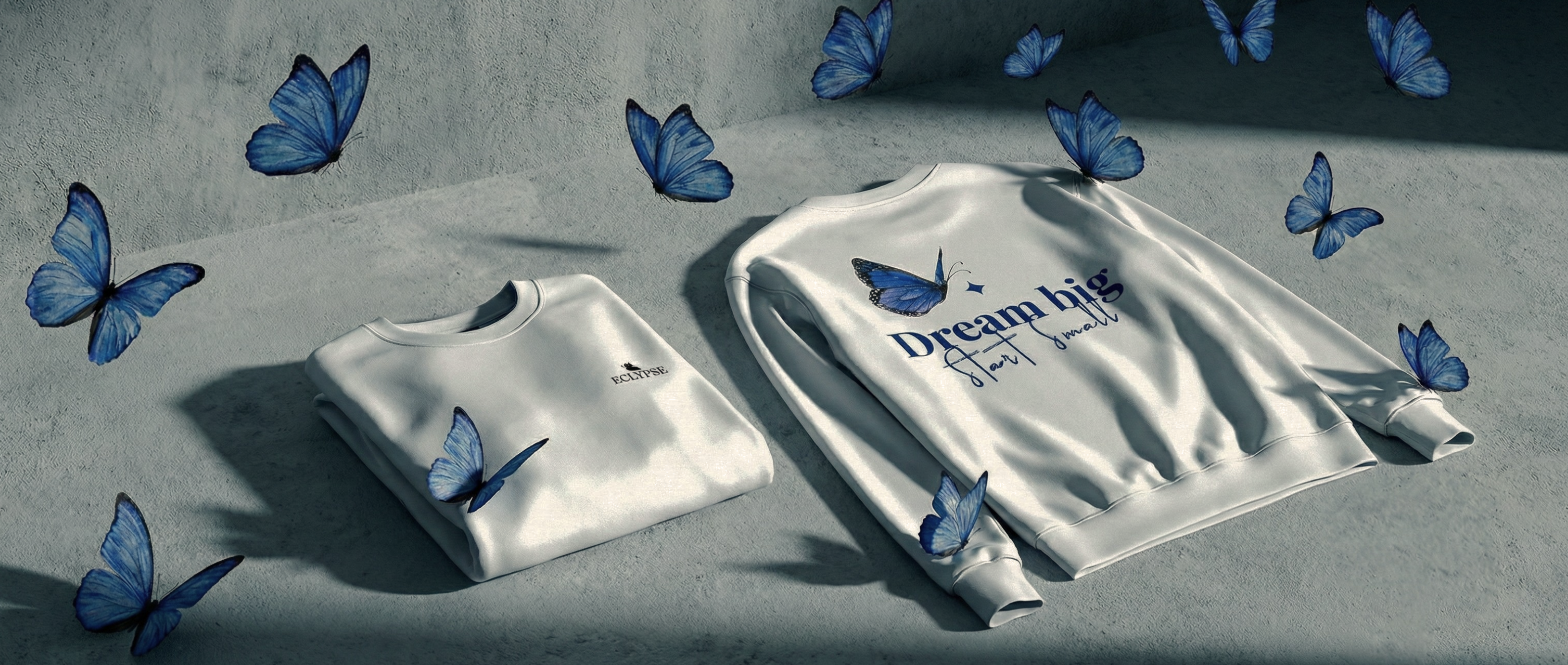 Sfeerbeeld van de Eclypse collectie met gevouwen witte sweaters, omringd door vliegende blauwe vlinders en de tekst Dream big start small.
